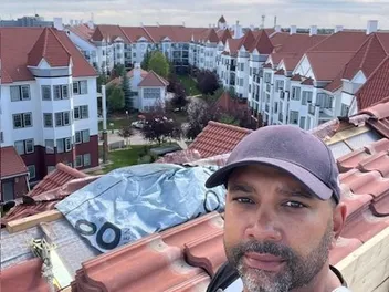 Crew member on the fire-damaged roof of a four-story condo building in Royal Oak NW, Calgary, with tarped openings